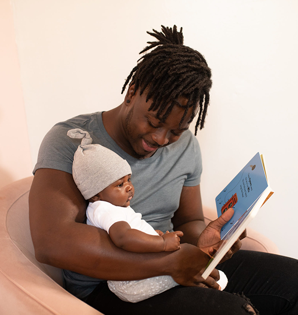 Ein Papa liest seinem kleinen Baby aus einem Pappbilderbuch vor.