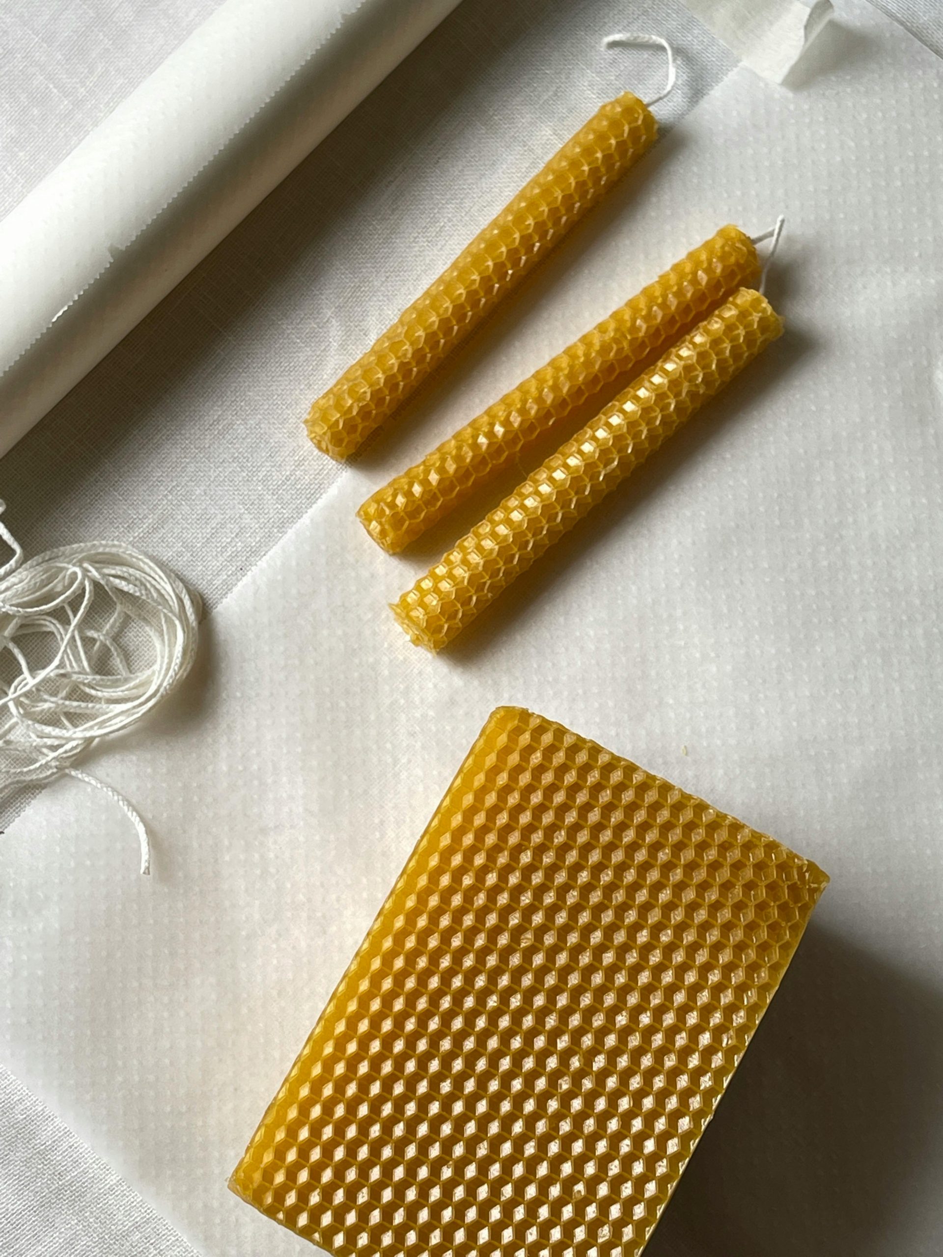 Auf dem Bild sind zwei Kerzen aus Bienenwachs und eine Bienenwachsplatte zu sehen.